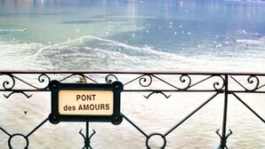 Un panneau indiquant « PONT des AMOURS », avec en arrière-plan un lac paisible et des montagnes lointaines.