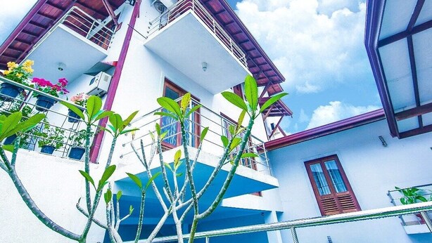 Un edificio de varios pisos con tejado rojo, balcones y un cielo azul despejado.