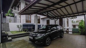 Un coche negro estacionado bajo una estructura cubierta, con un edificio blanco al fondo.