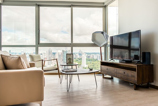 A modern living room with a large window, a sofa, a coffee table, a TV, and a lamp.