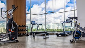 Een sportschool met cardioapparatuur, een wandrek met halters en een stadszicht door grote ramen.