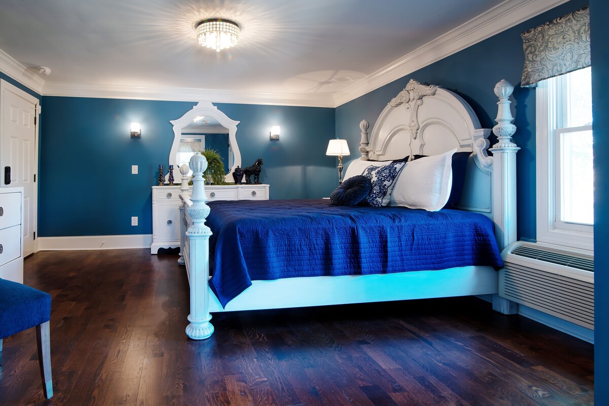 A bedroom with a large bed, a dresser, a mirror, and a window with curtains.