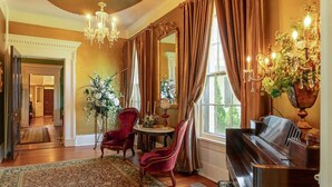 Un'ampia sala con un pianoforte, sedie rosse, un lampadario e un grande specchio.