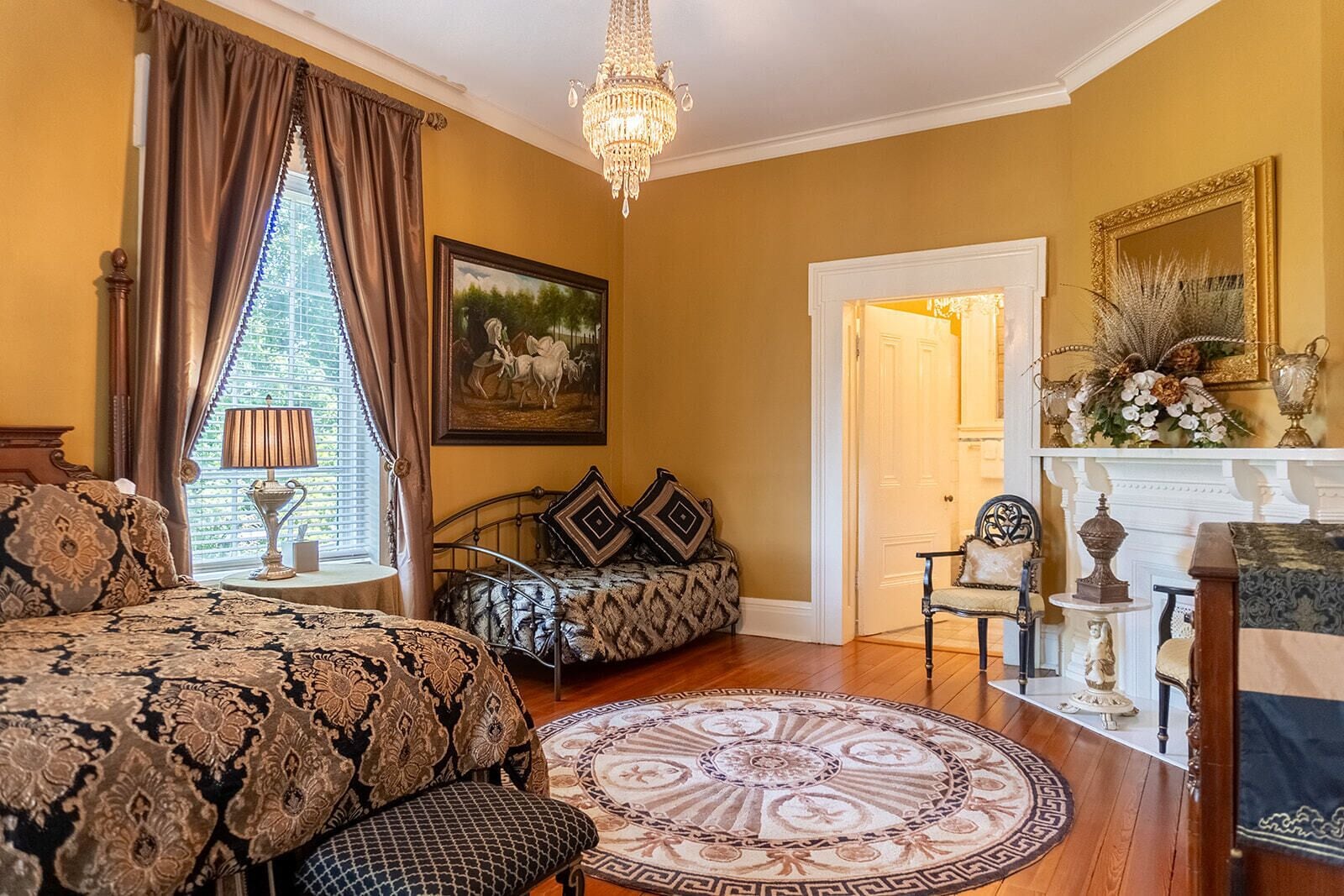 Ein traditionell eingerichtetes Schlafzimmer mit einem großen Bett, einem kleinen Sofa, einer Kristallleuchter und einem Kamin.