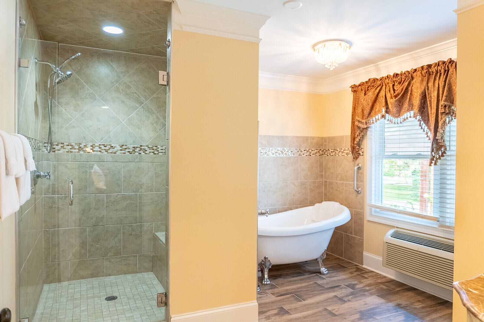 Un baño con ducha de vidrio, bañera independiente y ventana con cortina decorativa.