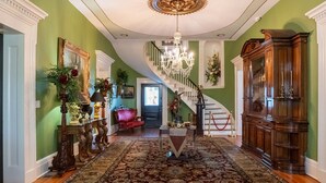 Un'imponente sala con un lampadario, una scala e una poltrona in pelle rossa.