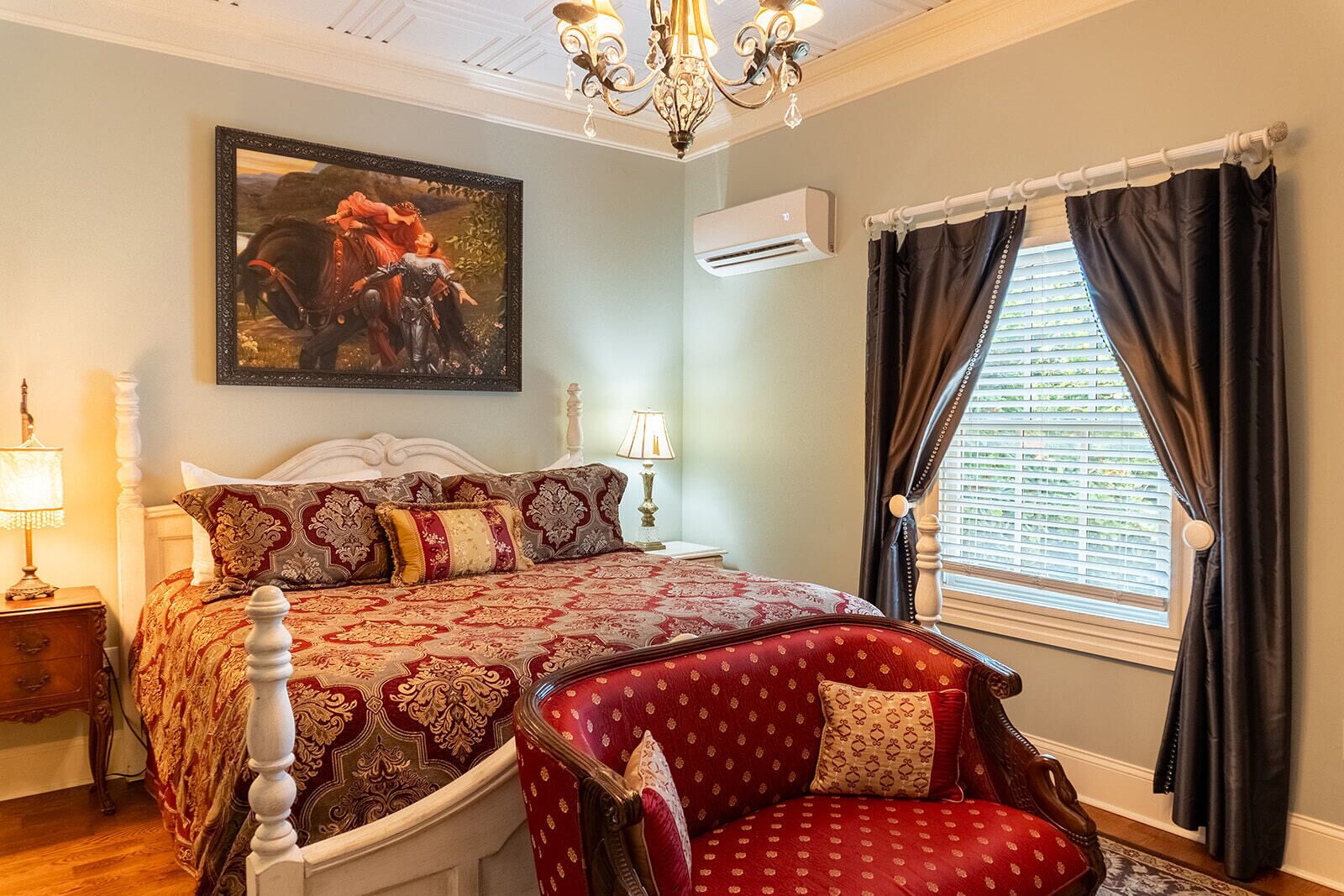 A bedroom with a large bed, a chair, a painting, and a window with curtains.