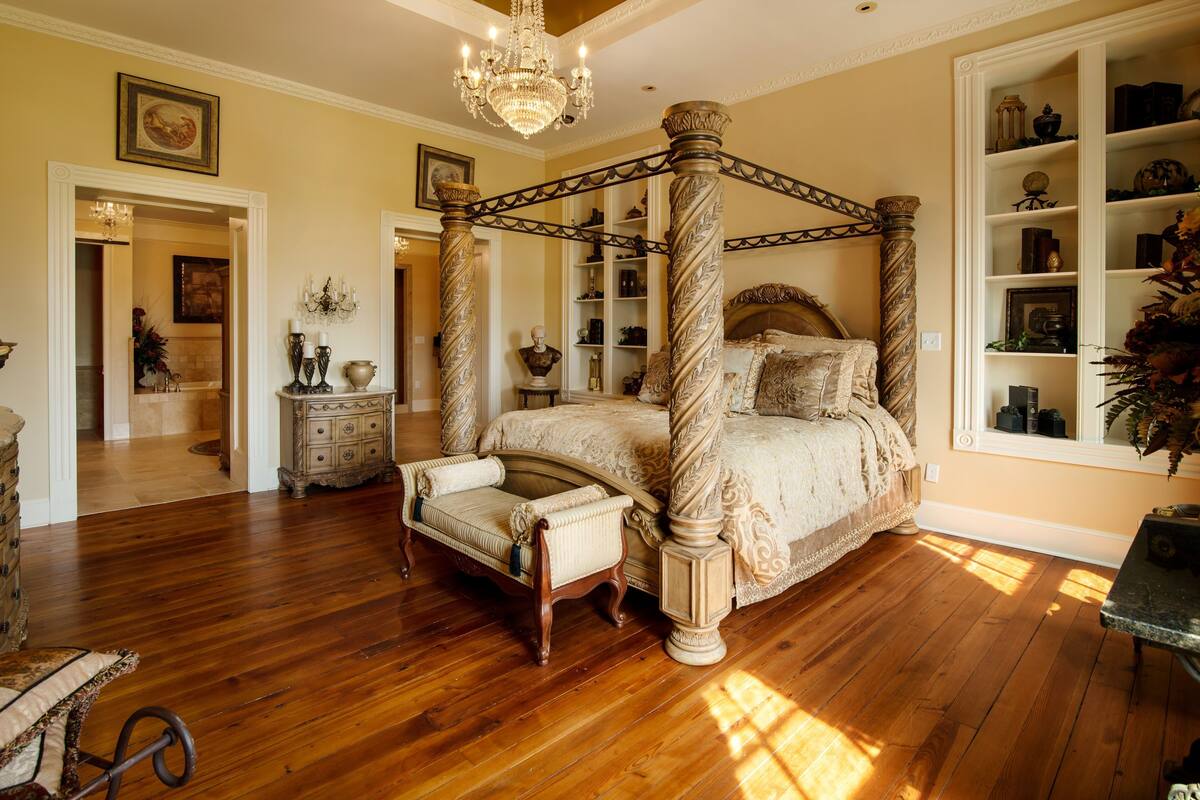 A spacious bedroom with a four-poster bed, wooden flooring, and a chandelier.