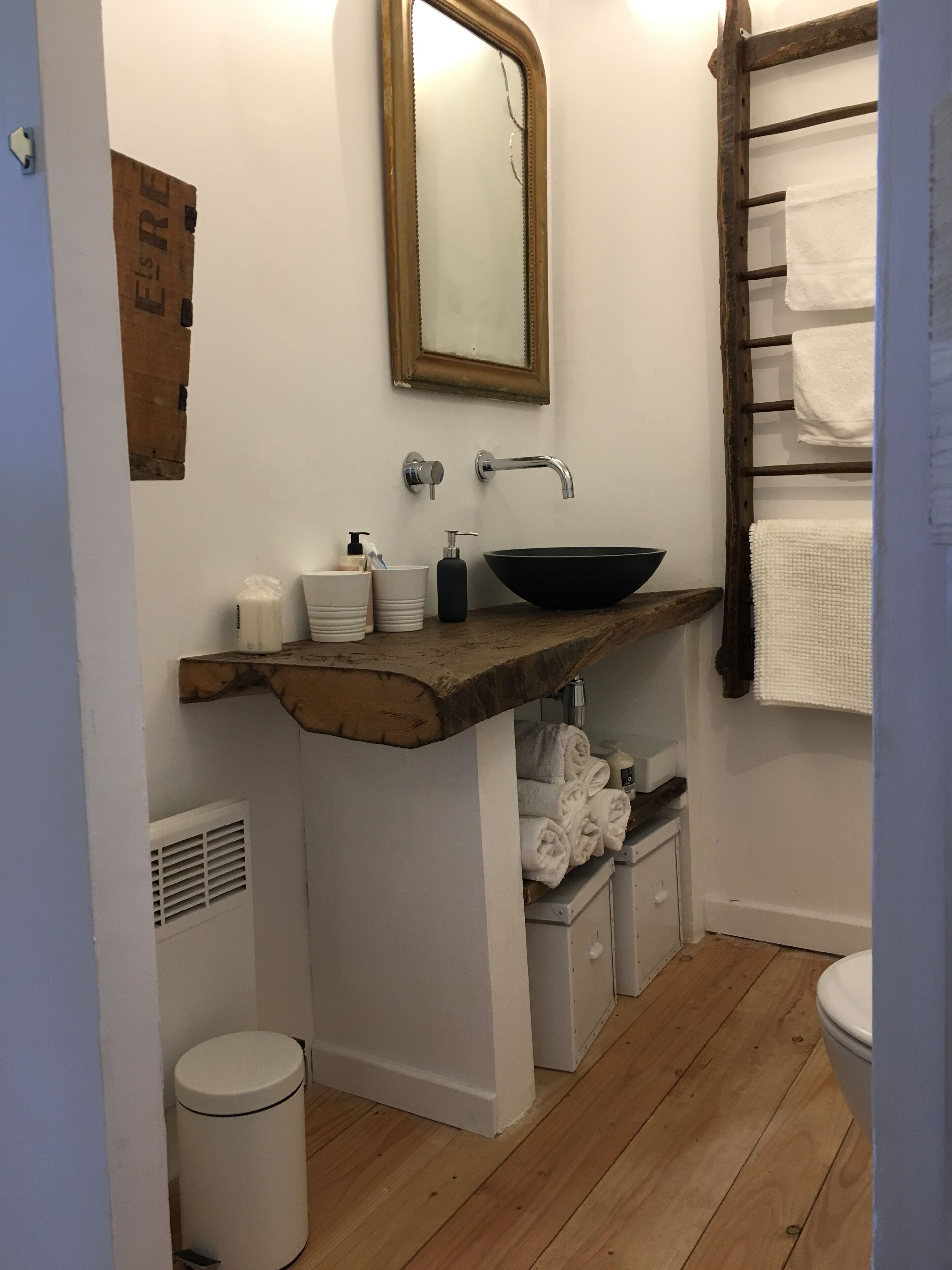 Un baño con tocador de madera, lavamanos negro, espejo y toallero.