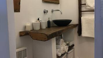 Un baño con tocador de madera, lavamanos negro, espejo y toallero.