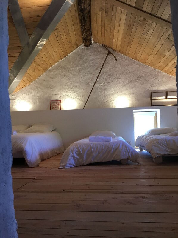 A cozy attic bedroom with wooden floors and sloped ceilings, featuring two beds and a small window. - Bergerie Cévennes " le SOUTOUL " swimming pool (2.5mX5.5m) (Dourbies)