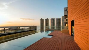 Una piscina en la azotea con vistas a la puesta de sol y edificios altos al fondo.