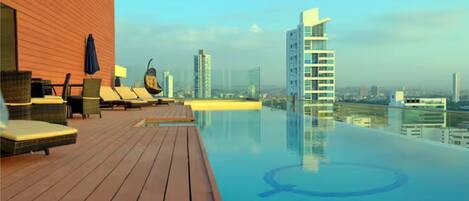 A rooftop infinity pool with lounge chairs and a wooden deck.