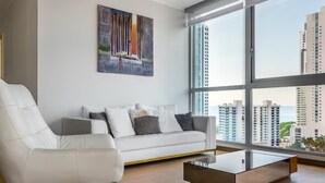 A modern living room with a white sofa, a glass coffee table, and a large window offering a city view.