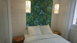Een slaapkamer met een bed, twee nachtkastjes, een muur met een tropisch bladpatroon en twee hanglampen.