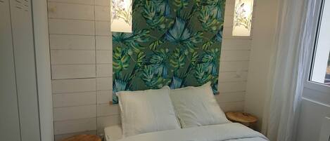 Quarto com cama, duas mesinhas de cabeceira, parede com padrão de folhagem tropical e duas luminárias pendentes.