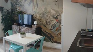 Een moderne keuken met een eethoek, met een witte tafel, turquoise stoelen, een zwart aanrecht en een muurschildering van tropische planten.