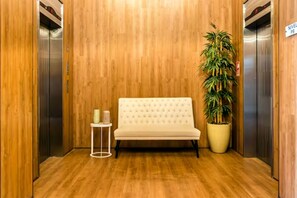 Eine Lobby mit Holzboden, einem weißen Sofa, einem kleinen Tisch und einer großen Topfpflanze.