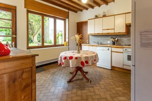 Una cucina con mobili in legno, un tavolo da pranzo con tovaglia a fiori e una finestra vista verde.