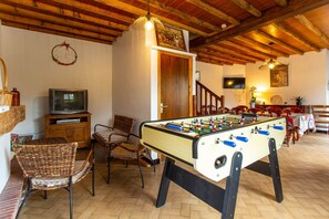 Una camera accogliente con un tavolo da calcio, una televisione, poltrone in vimini e un soffitto in legno.