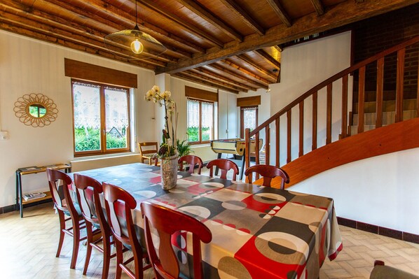 Un'area pranzo con un tavolo e sedie in legno, un vaso con fiori e vista sull'esterno attraverso ampie finestre.