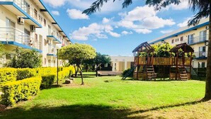 Un pati amb un parc infantil, garedes ben tallades i un edifici d'alguns pisos amb balcons.
