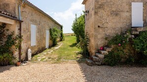 A narrow gravel path leading through a rustic stone building with white shutters, surrounded by greenery and a clear sky. - The Clos Jacquet house of 180 m2 (GUILLAC)