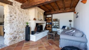 A rustic living room with exposed wooden beams, a stone wall, a fireplace, a television, and a grey sofa. - The Clos Jacquet house of 180 m2 (GUILLAC)