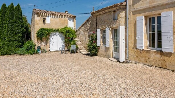 A courtyard with a gravel ground, a stone building with a white door, and a small table with chairs. - The Clos Jacquet house of 180 m2 (GUILLAC)