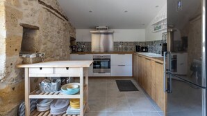 A kitchen with stone walls, a wooden table, a built-in oven, and a stainless steel refrigerator. - The Clos Jacquet house of 180 m2 (GUILLAC)