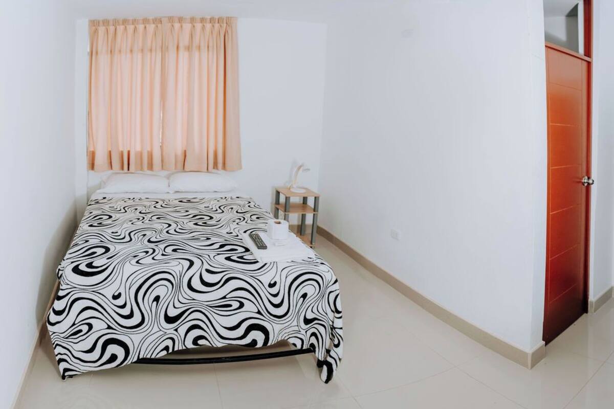 A bedroom with a bed, a nightstand, a window with curtains, and a door.