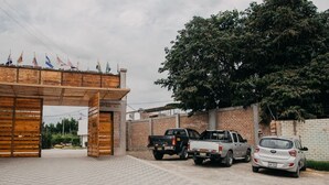 Una entrada con reja y un arco de madera, un camino pavimentado y vehículos estacionados, incluyendo una camioneta Toyota y un auto Hyundai.