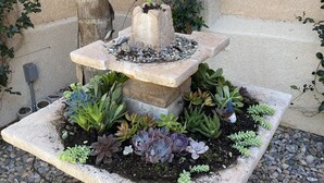 A stone fountain with a tiered design, surrounded by various succulents and plants, set on a bed of pebbles. - Perfect Escape - Festival close, on golf course, private salt water pool, +++! (Indio)