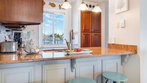 A kitchen with a granite countertop, stainless steel appliances, and a window with blinds.