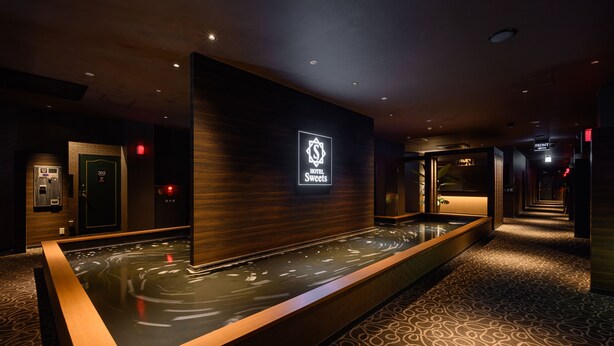 Un hall d’hôtel comprenant un comptoir d’accueil, un panneau d’affichage numérique et un élément décoratif aquatique.