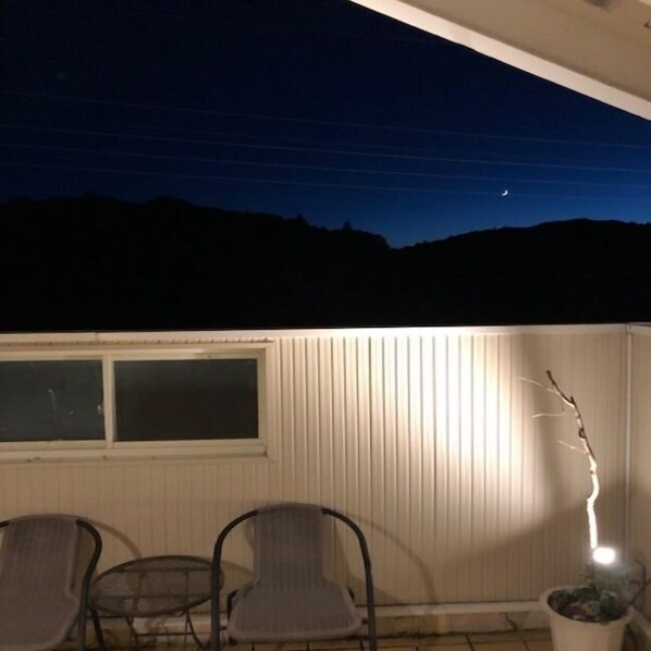 Un patio con mesa y sillas, una planta en maceta y una ventana con vista a un paisaje oscuro.