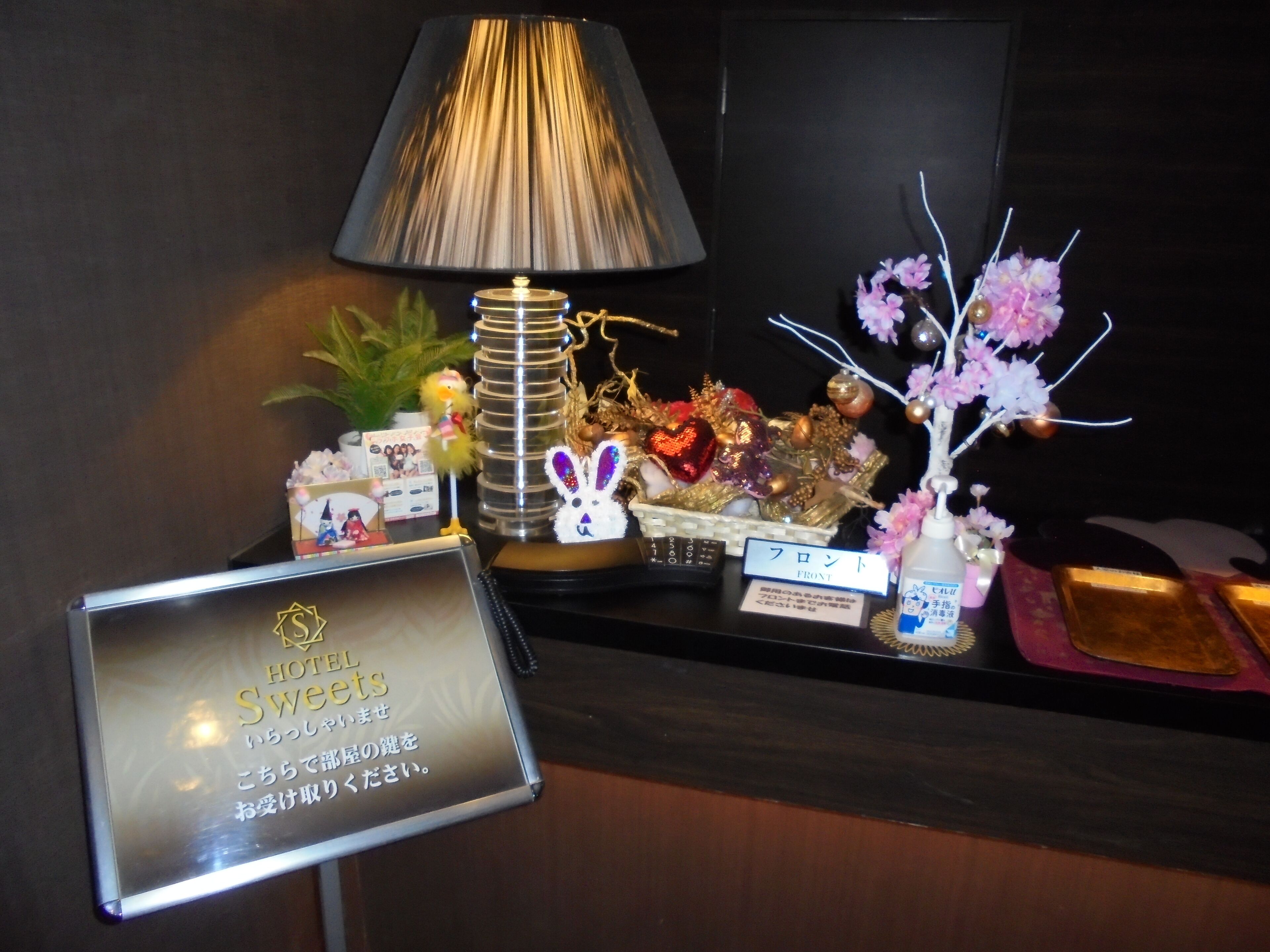 A hotel reception desk with a sign for 'Hotel Sweetets', a lamp, decorative items, and a small sign indicating 'Front'.