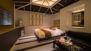 Une chambre moderne avec un lit, une table basse en verre ornée de fleurs, un canapé en cuir noir et un design de plafond original.