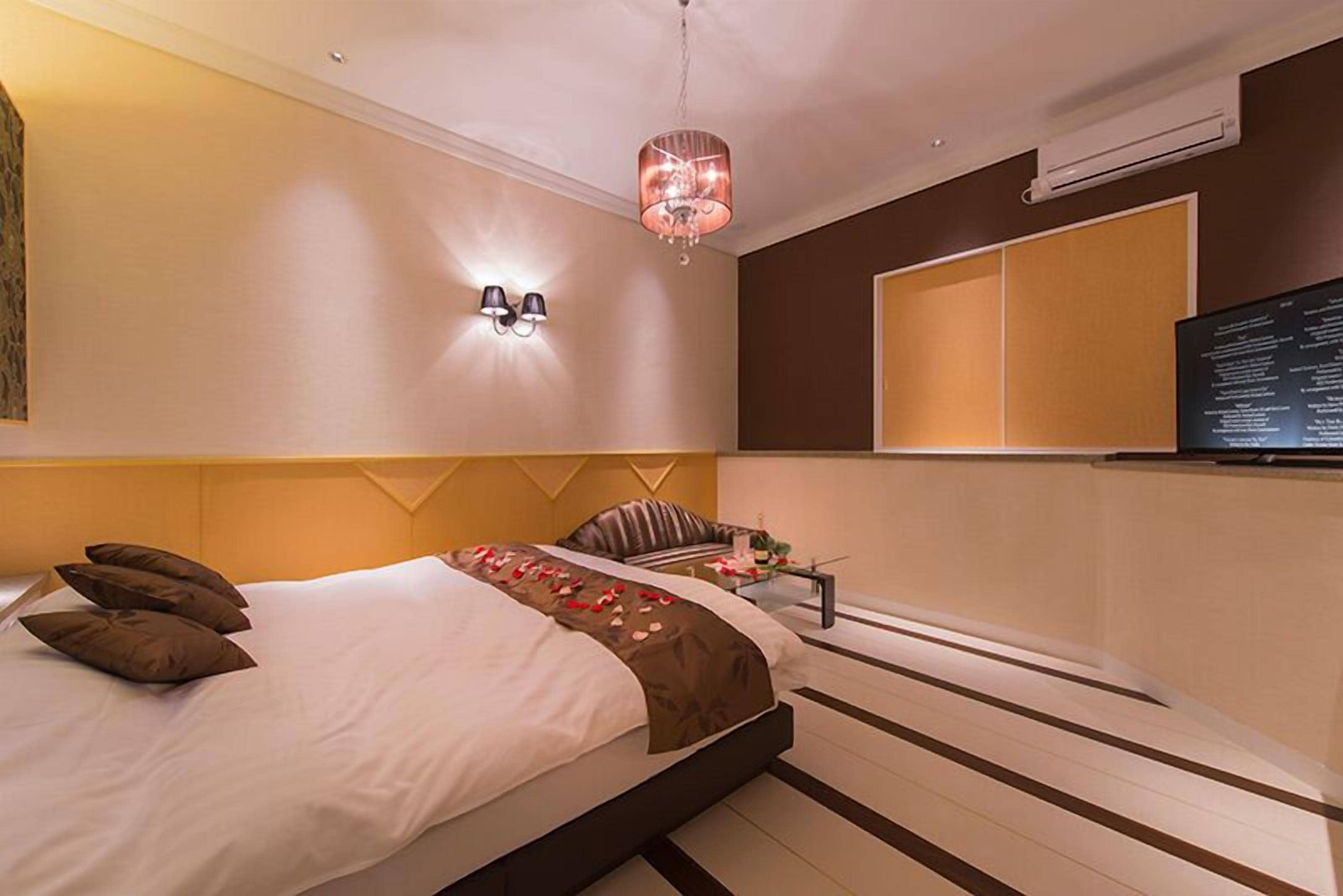Une chambre d’hôtel moderne dotée d’un grand lit, d’un petit coin salon, d’un téléviseur fixé au mur et d’un luminaire décoratif.