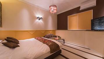 Une chambre d’hôtel moderne dotée d’un grand lit, d’un petit coin salon, d’un téléviseur fixé au mur et d’un luminaire décoratif.