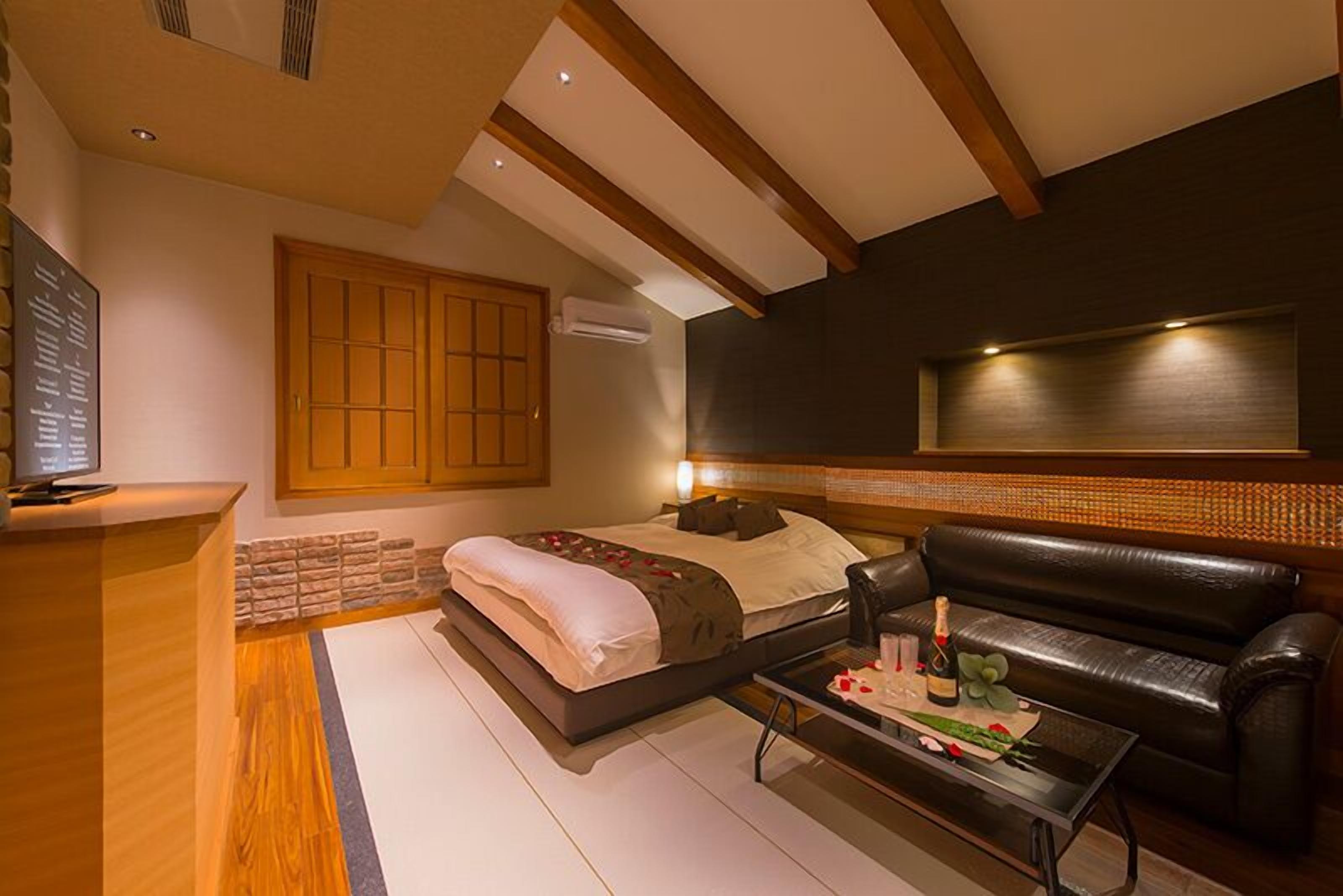 Quarto de hotel moderno com cama, sofá, mesa de centro e televisão.