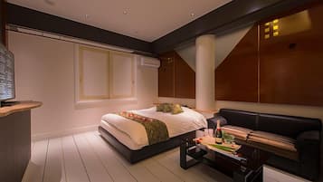 Quarto moderno com uma cama grande, um sofá de couro preto, uma mesa de centro de madeira e uma TV sobre um suporte.