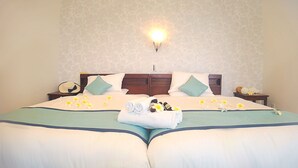 A neatly made bed with a floral-patterned wall, a bedside lamp, and a nightstand with a hat and sunglasses. - Ecot Shimozato 1 (Miyakojima)