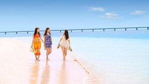 Three women walking on a beach with a pier in the background. - Ecot Shimozato 1 (Miyakojima)