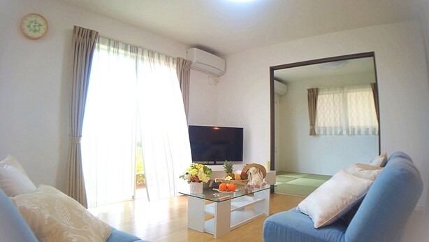 A living room with a flat-screen TV, a glass coffee table, and two blue sofas. - Ecot Shimozato 1 (Miyakojima)
