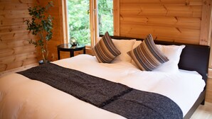 Un dormitorio de cabaña de madera con una cama grande, una mesita de noche y una ventana con vistas al verdor.