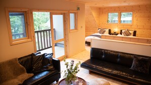 Una habitación acogedora con techo de madera, un sofá de cuero negro, un banco blanco y una mesita con un jarrón.