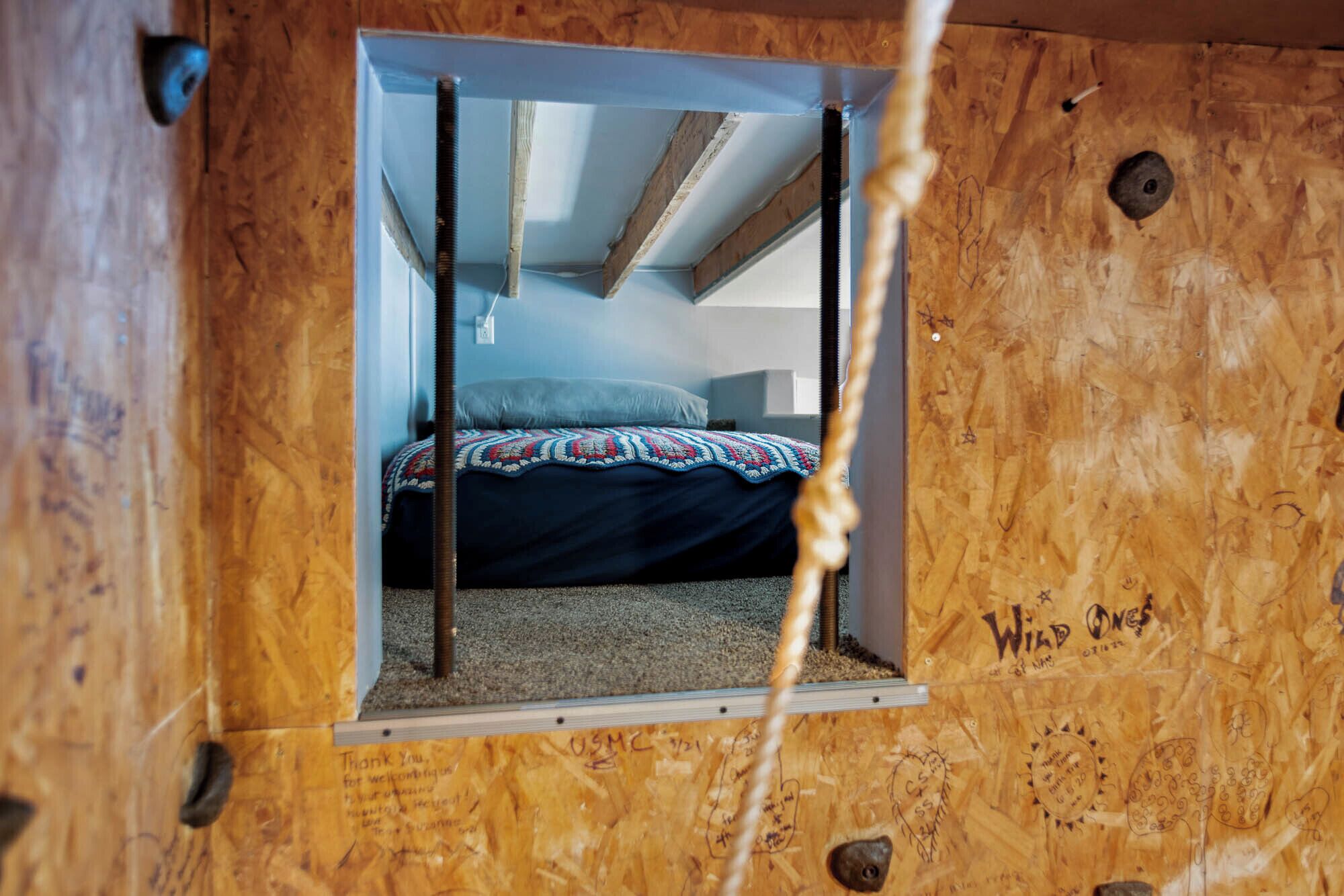 A small, enclosed room with a bed, a window, and wooden walls.