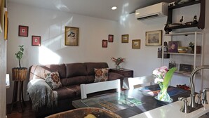 A living room with a brown sofa, a coffee table, and a kitchen area with a sink and faucet.