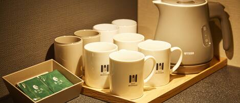 Un juego de tazas blancas con el logotipo de un hotel, un juego de té y una caja de té verde sobre una bandeja de madera.
